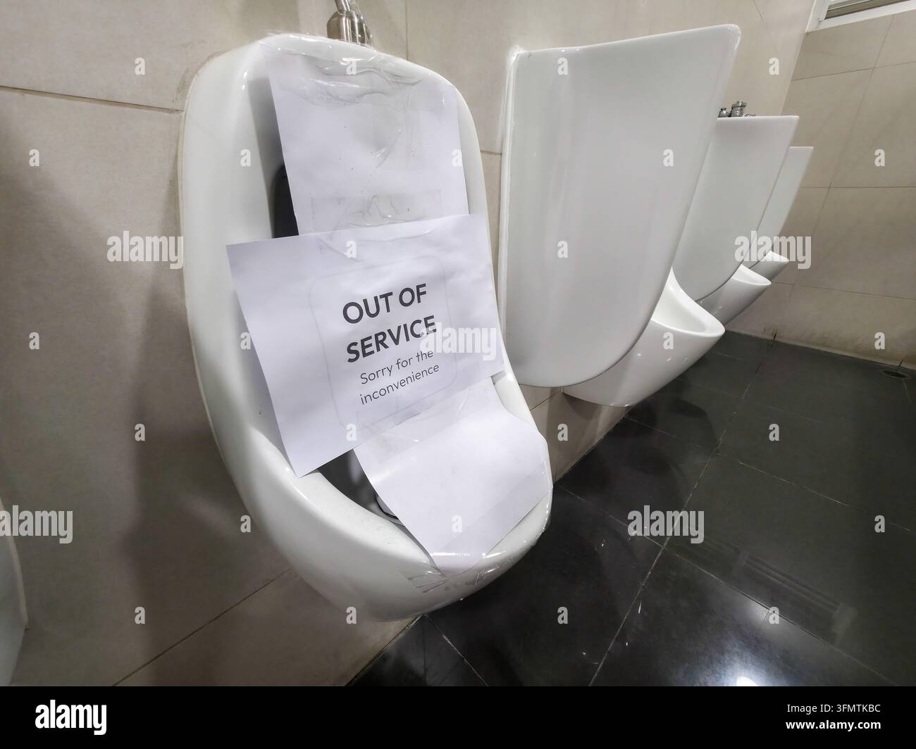Ein außer Betrieb gesetztes Urinal, das in einer öffentlichen Toilette mit Schutzpapier abgedeckt ist, zeigt Wartungsschließung und nicht verfügbare Sanitärausrüstung Stockfoto