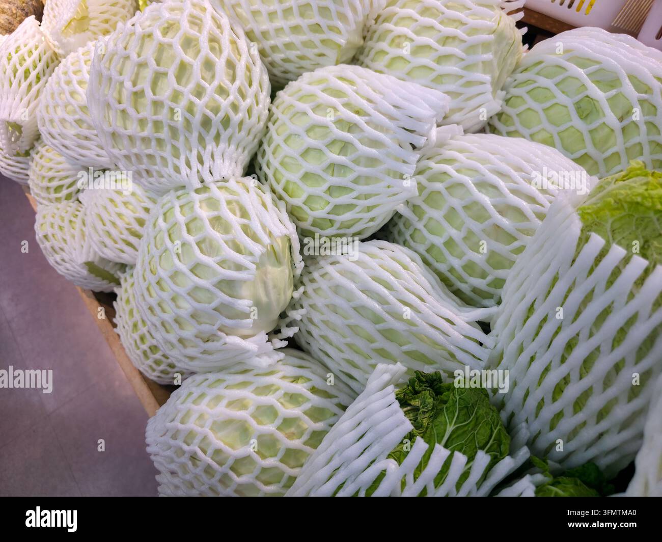 Ein weißer Melon in schützendem Schaumstoffnetz auf dem Marktstand, der frisches hellgrünes Fruchtfleisch, eine strukturierte Hülle und sorgfältige Verpackung der Produkte zeigt Stockfoto