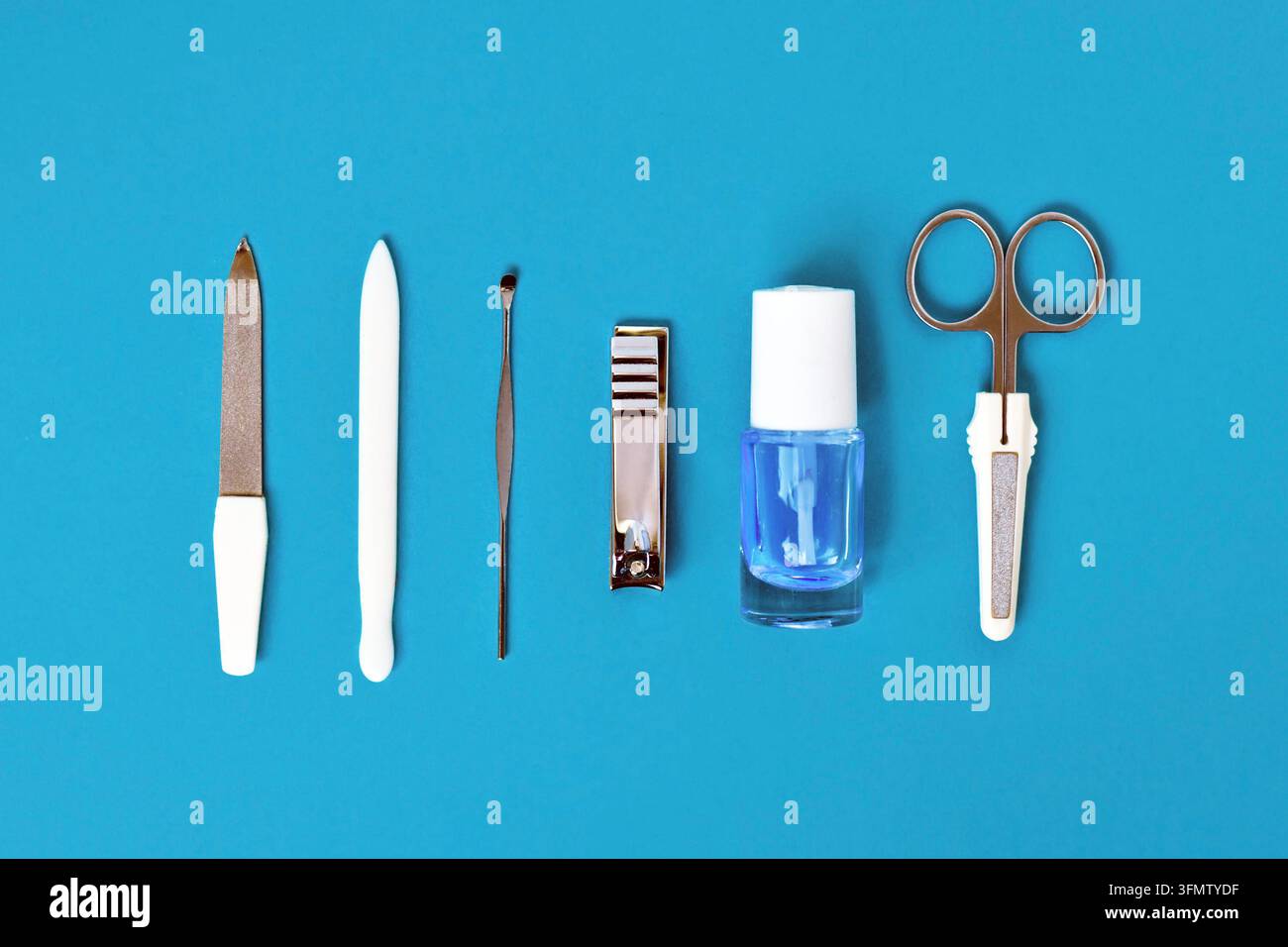 Maniküre-Set und Nagellack in einer Reihe auf blauem Hintergrund angeordnet Stockfoto
