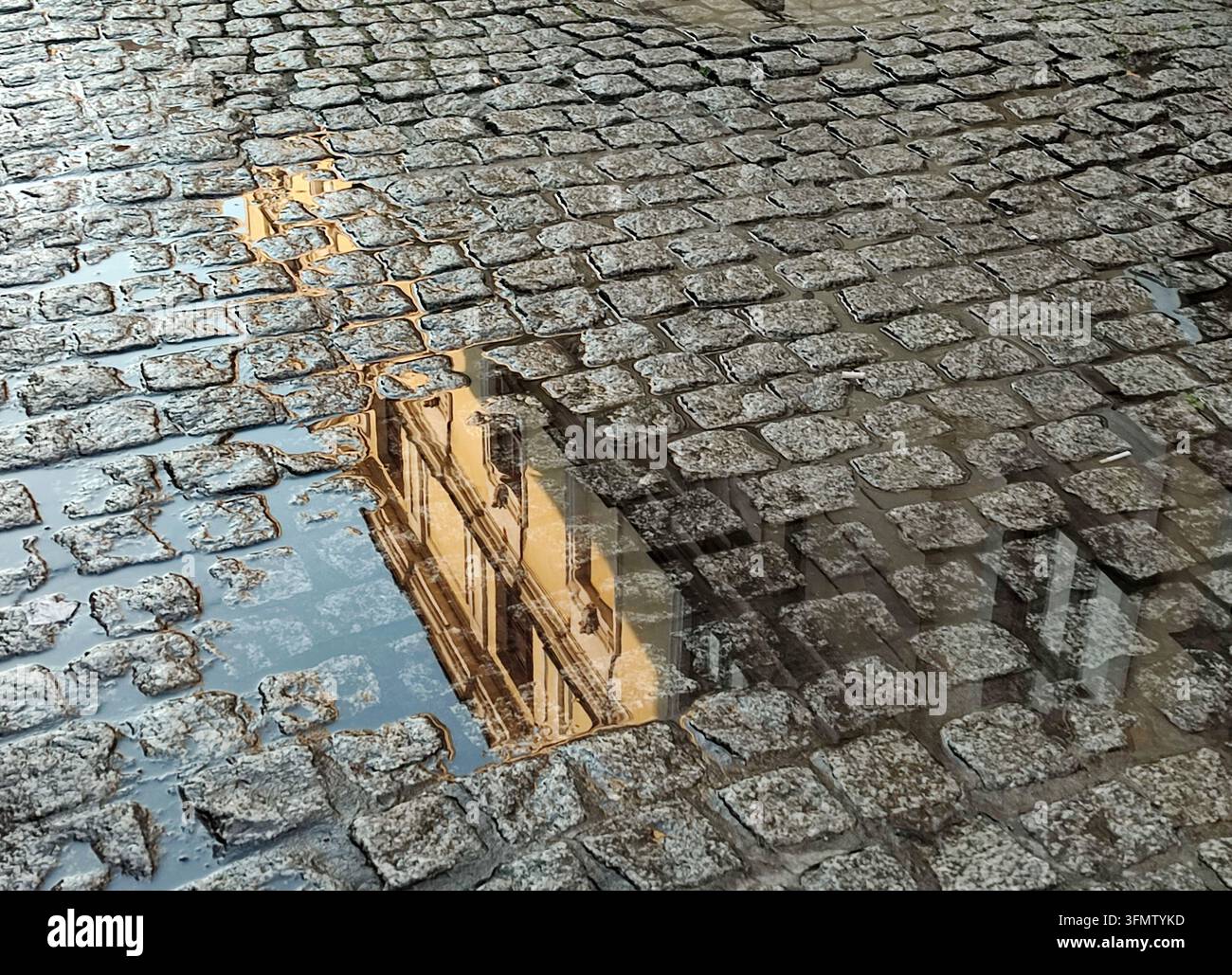 Historisches Gebäude, das sich in einer Regenpfütze auf einer traditionellen Kopfsteinpflasterstraße in Krakau, Polen, spiegelt. - Smartphone-aufgenommenes Stockfoto