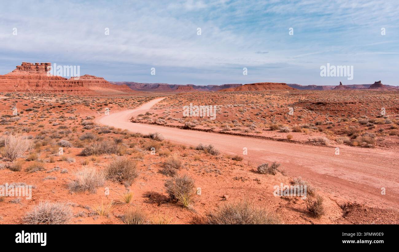 Schotterstraße windet sich durch farbenfrohe Felsformationen und Buschland im Tal der Götter nahe Mexican Hat, Utah. Stockfoto