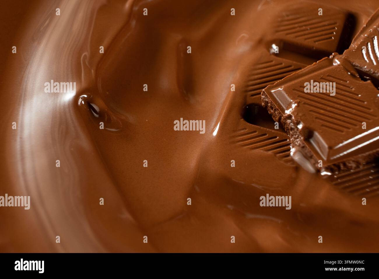 Schokoladenstücke, die zu glatter, warmer Schokoladenflüssigkeit schmelzen, Makroaufnahme. Stockfoto