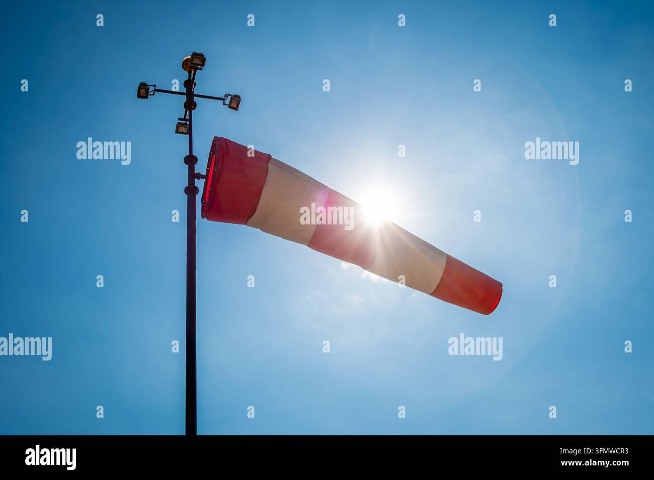 Rot-weißer Windsack, vom Wind aufgebläht, von der Sonne beleuchtet vor blauem Himmelshintergrund. Konzepte der Wettervorhersage, Windrichtung und Wi Stockfoto