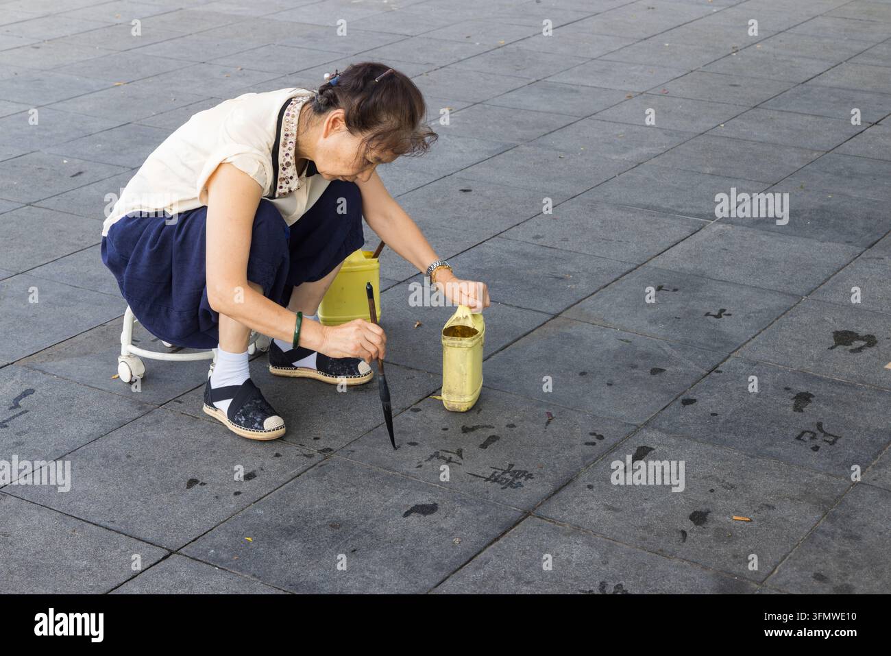 Eine Frau praktiziert chinesische Kalligraphie, indem sie Schriftzeichen im Wasser auf dem Pflaster in Xi'an, China, schreibt Stockfoto