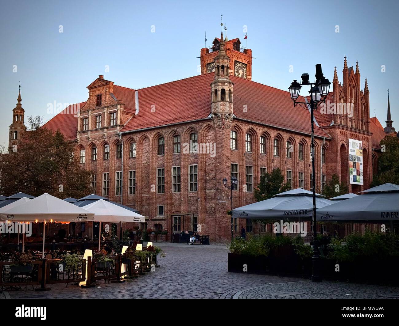 Weitwinkelaufnahme des historischen gotischen Rathauses aus rotem Backstein (Ratusz Staromiejski) auf dem Kopfsteinpflasterplatz in Toruń, Polen, umgeben von Straßencafés - Smartphone-aufgenommenes Stockfoto