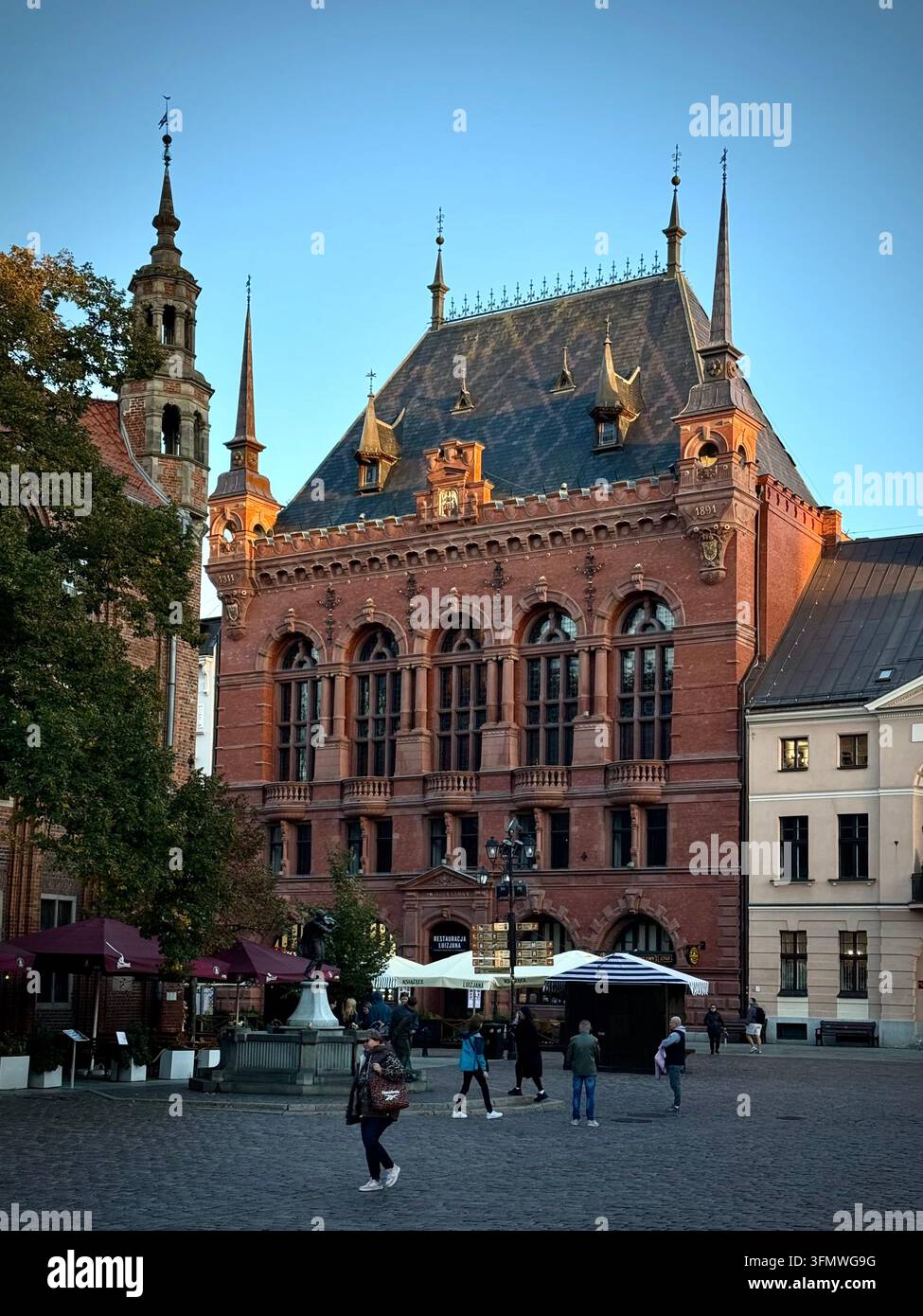 Vertikale Ansicht des historischen roten Backstein-Neorenaissance-Artus-Hofes auf dem Kopfsteinpflaster des Altstadtmarktes in Toruń, Polen. - Smartphone-aufgenommenes Stockfoto