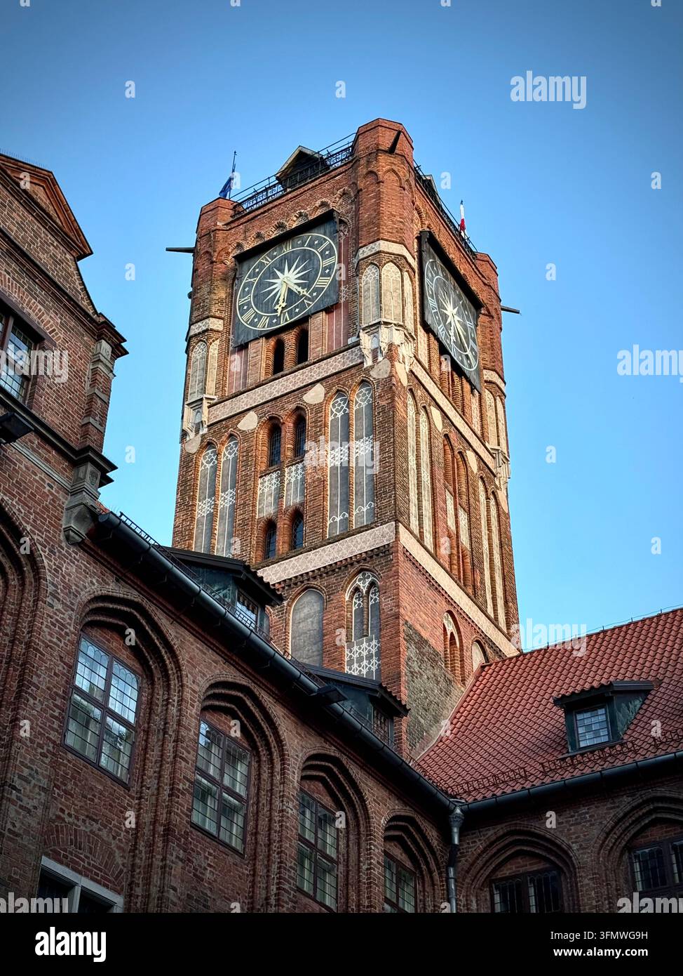 Vertikale Blickwinkelaufnahme des historischen roten gotischen Rathauses-Turms mit großen Uhrzifferblättern vor einem blauen Himmel in Thorn, Polen. - Smartphone-aufgenommenes Stockfoto