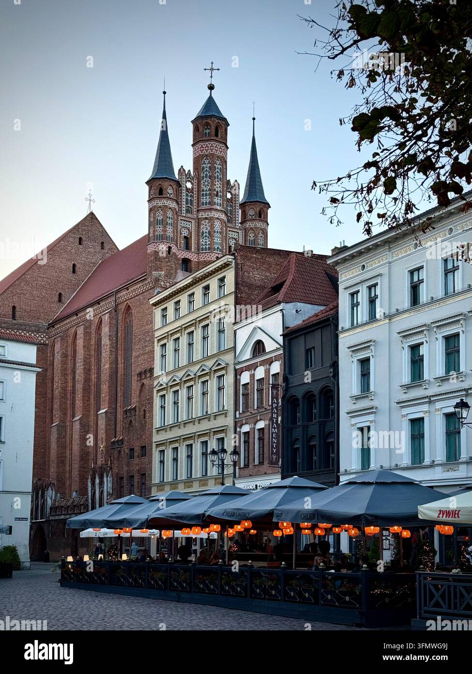 Vertikale Ansicht entlang der Żeglarska Straße in Richtung des gotischen Turms der St.-Johannes-Kathedrale über historischen Stadthäusern und einer Außenterrasse eines Cafés in Toruń - Smartphone-aufgenommenes Stockfoto