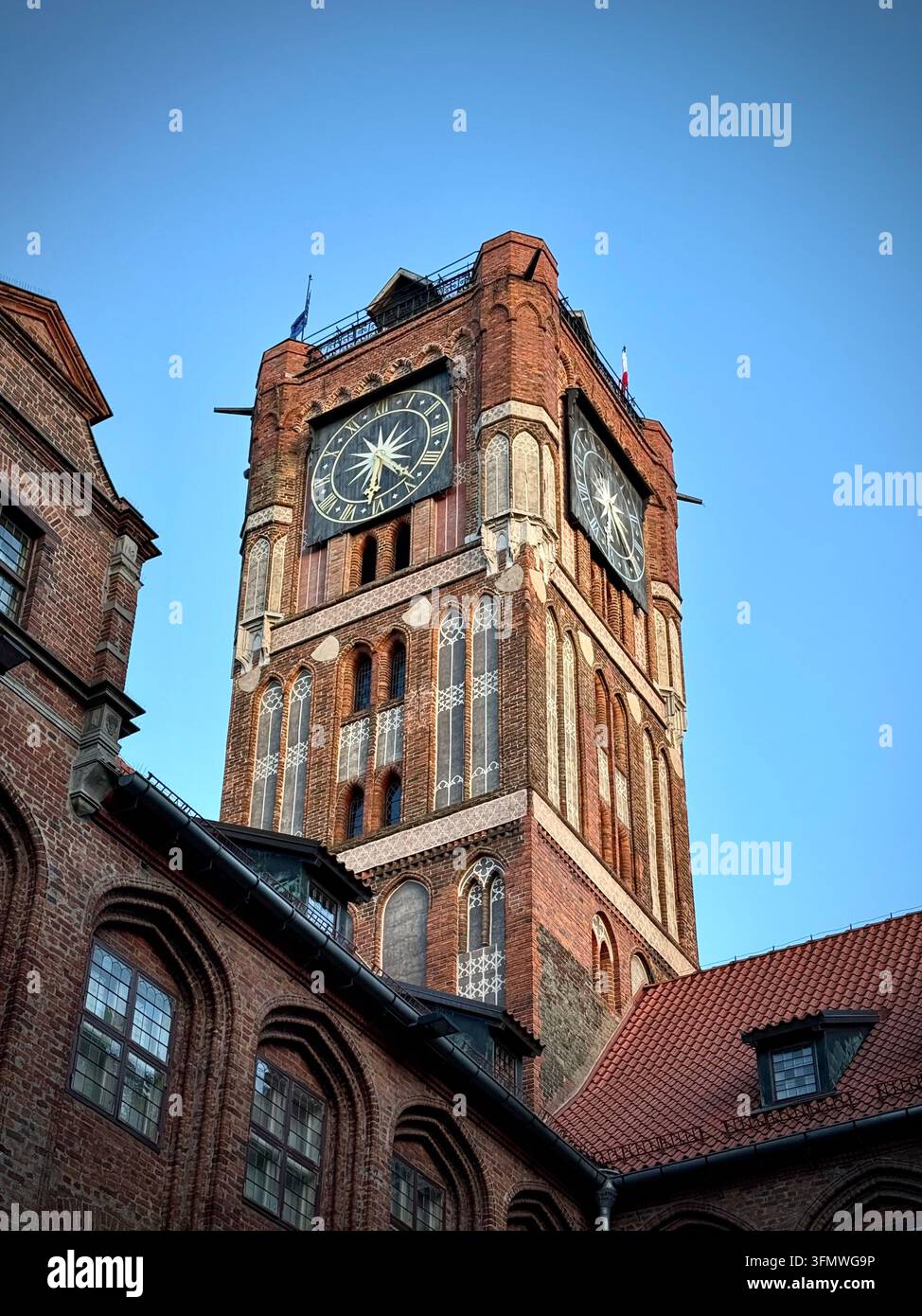Vertikale Blickwinkelaufnahme des historischen roten gotischen Rathauses-Turms mit großen Uhrzifferblättern vor einem blauen Himmel in Thorn, Polen. - Smartphone-aufgenommenes Stockfoto