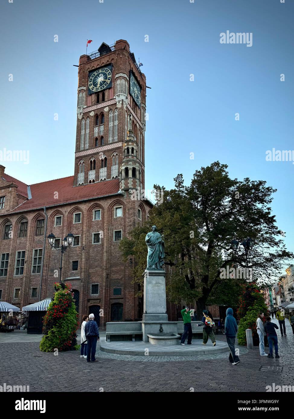 Vertikale Ansicht des Nicolaus-Copernicus-Denkmals und des gotischen roten Backsteinturms des Alten Rathauses auf dem Kopfsteinpflaster des Alten Marktplatzes in Thorn - Smartphone-aufgenommenes Stockfoto