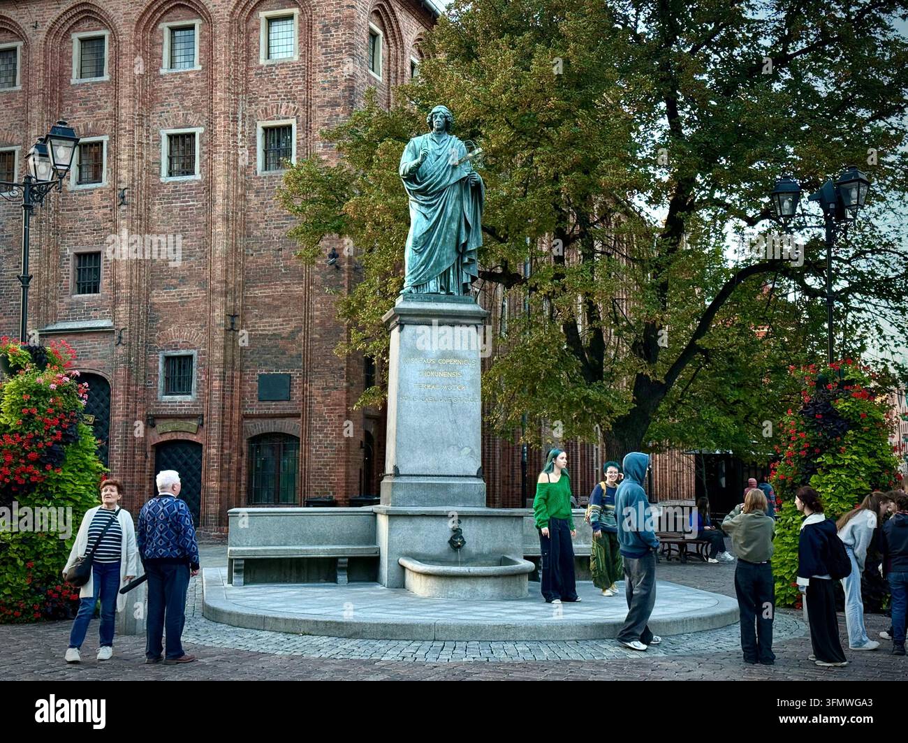 Ansicht des bronzenen Denkmals für Nicolaus Kopernikus vor dem roten Backstein-Rathaus auf dem Kopfsteinpflaster des Altmarktplatzes in der Altstadt von Toruń, Polen. - Smartphone-aufgenommenes Stockfoto