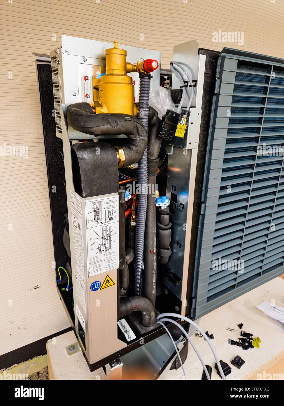 Offene Außeneinheit einer Wärmepumpe mit isolierten Kältemittelleitungen, Kupferrohren, elektrischen Anschlüssen und internen mechanischen Komponenten während der Insta Stockfoto