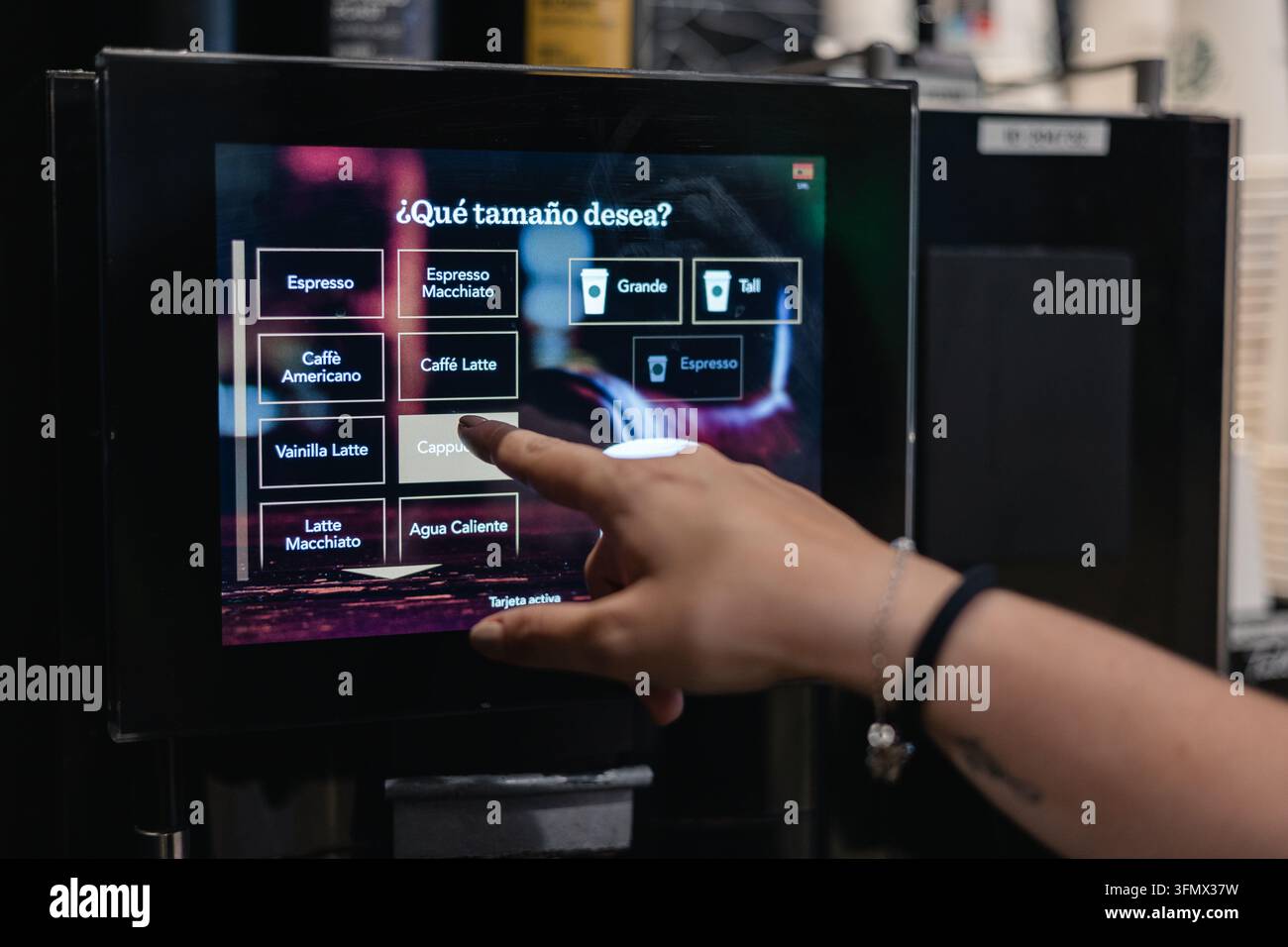 Kunde wählt Cappuccino an einem interaktiven Touchscreen-Kaffeevollautomaten, nutzt automatisierte Selbstbedienungstechnologie Stockfoto