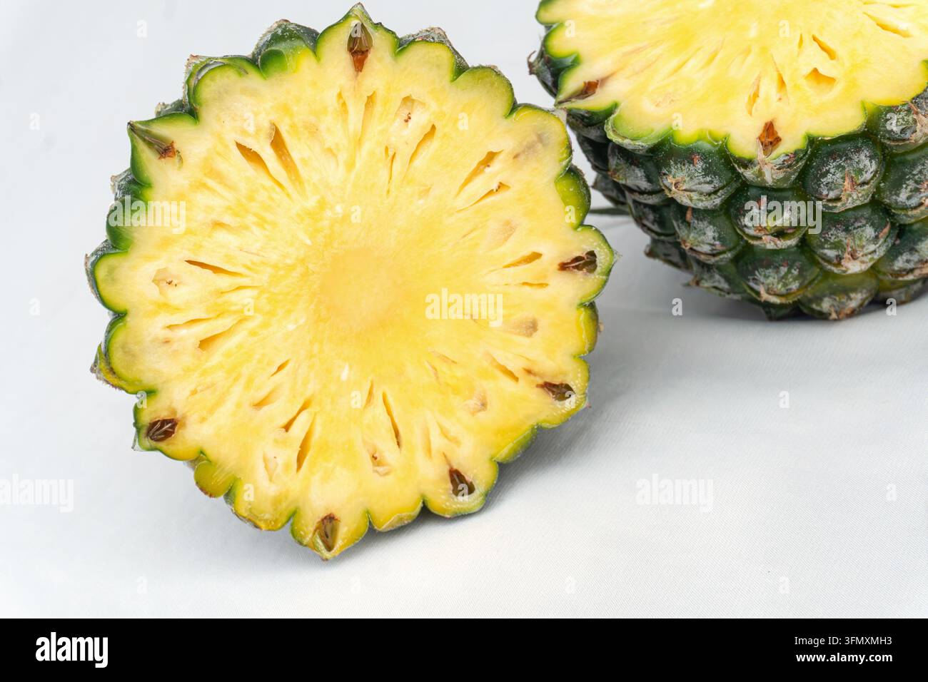 Ananas in der Hälfte geschnitten, der gelbes faseriges Fleisch und grüne Schale zeigt, neben einem ganzen Ananas auf weißem Studiohintergrund Stockfoto