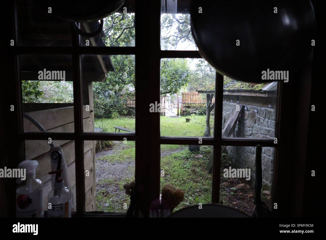 Fensterblick aus einem rustikalen Raum mit Blick auf einen Garten und eine Steinmauer. Stockfoto