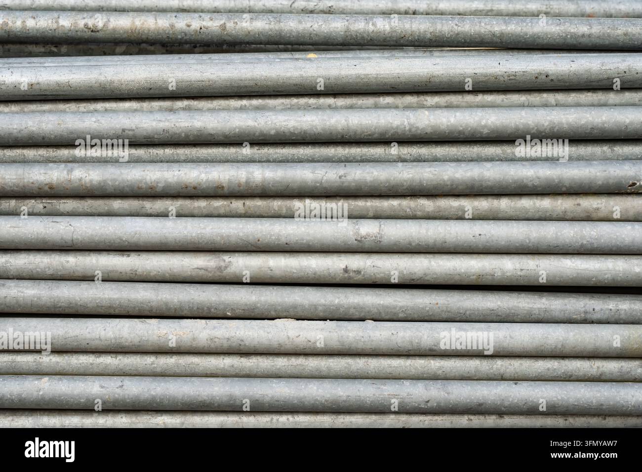 Ein gelagertes Bündel verwitterter verzinkter Rohre zeigt wiederholte Längen und abgenutzte Metallbeschichtungen, die Baurohrbestände und Inspektionen repräsentieren Stockfoto