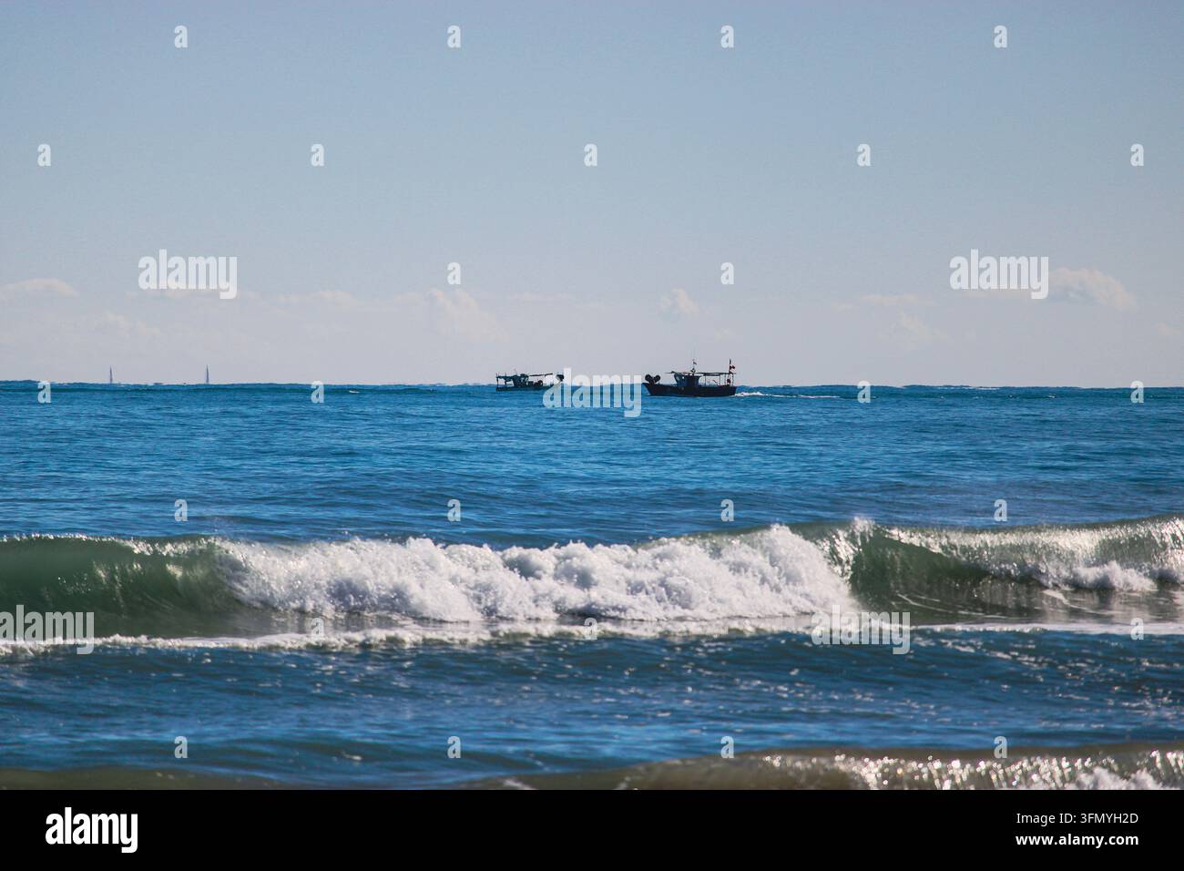 Brachende Meereswellen mit weißem Schaum rollen unter einem klaren blauen Himmel auf das Ufer zu. Stockfoto