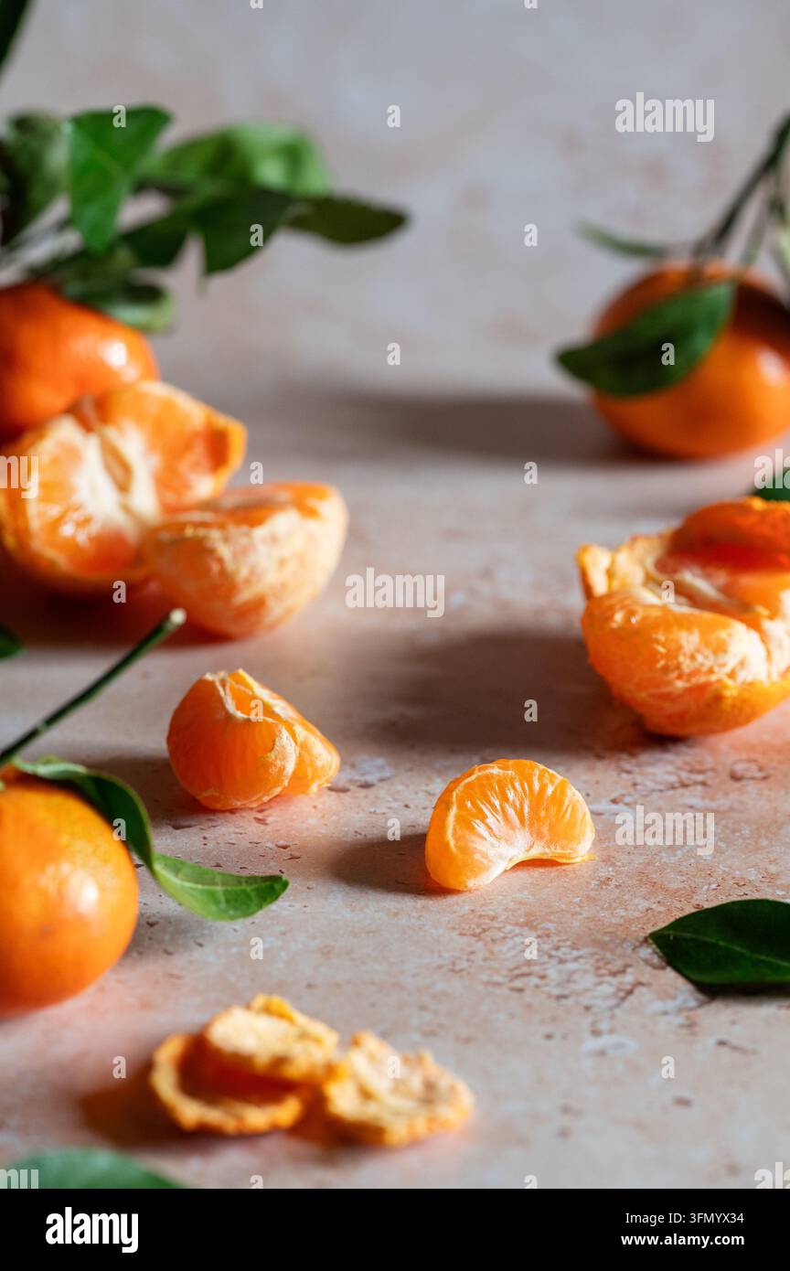 Frische Mandarinen mit geschälten Segmenten, einer Kurve der Schale und grünen Blättern, die auf einem rustikalen Steintisch arrangiert sind, und die ein lebendiges Zitrus-Stillleben mit natu Stockfoto