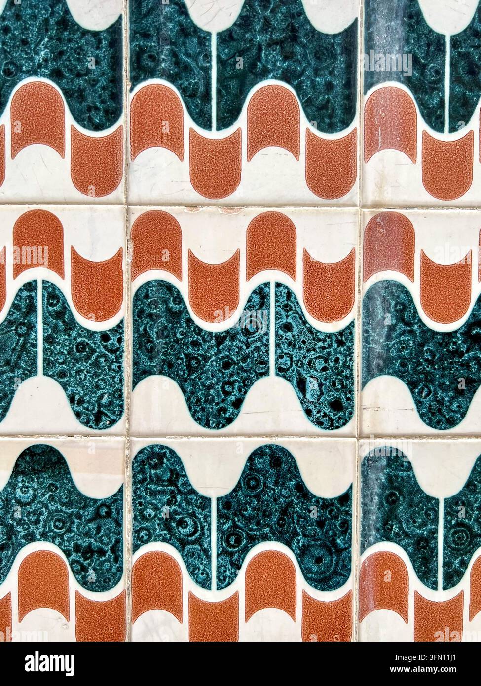Portugiesische Azulejo-Wandfliesen in Portugal mit sich wiederholenden blaugrünen und orangefarbenen Wellenformen auf einer cremefarbenen Glasur - Smartphone-aufgenommenes Stockfoto