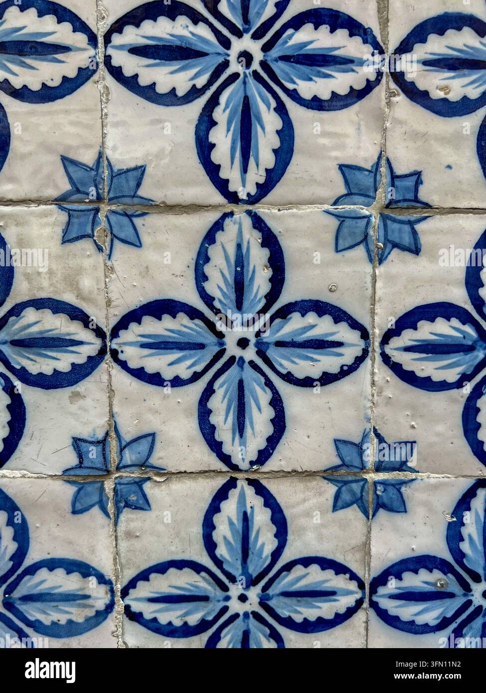 Alte blau-weiße Azulejo-Fliesen mit einem handbemalten vierblättrigen Blumenmuster an einer verwitterten Wand in Portugal - Smartphone-aufgenommenes Stockfoto