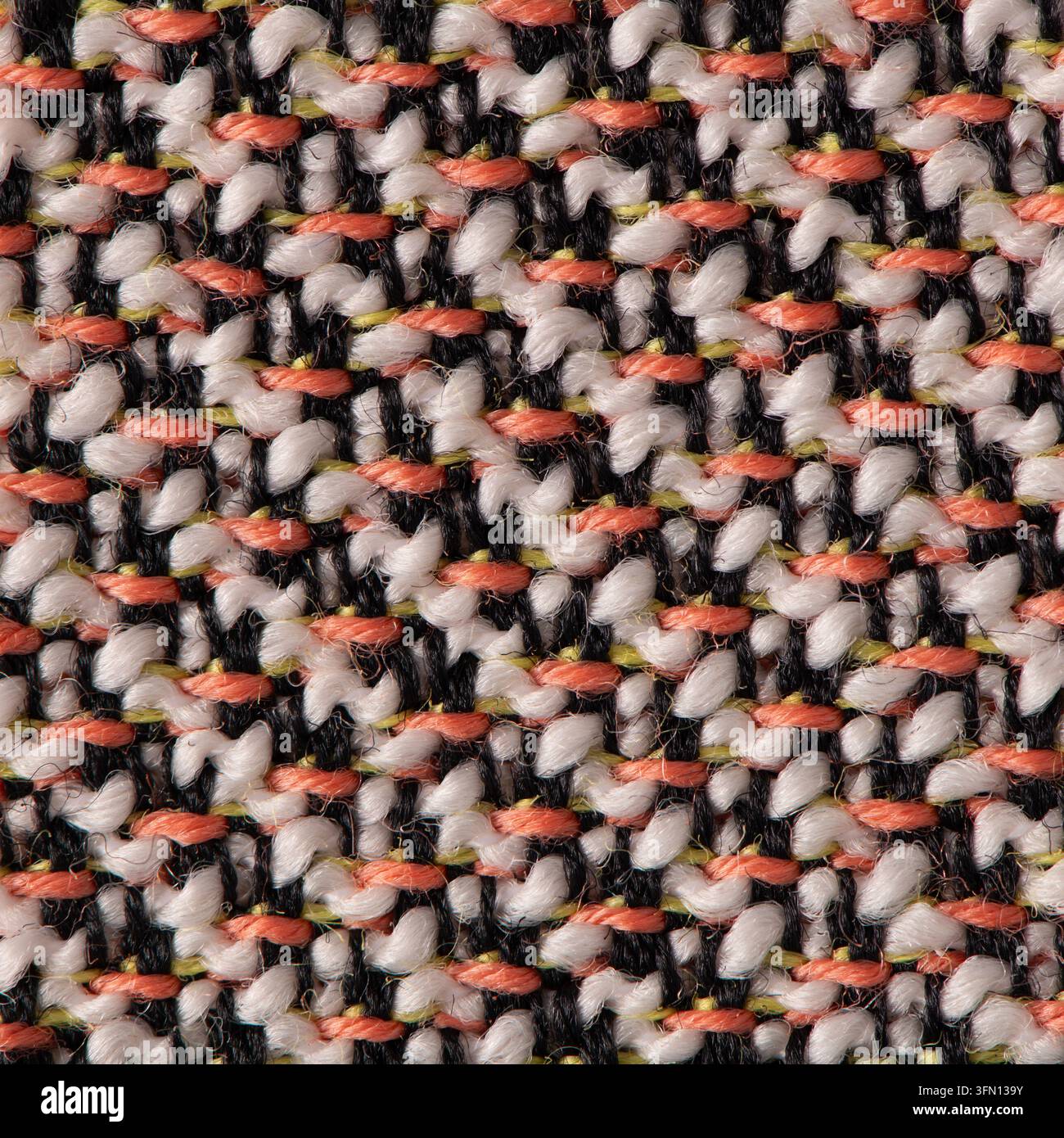 Makroaufnahme von dick gewebtem Tweedstoff mit verflochtenen rosa, schwarzen und weißen Fäden bei weicher Beleuchtung, die das haptische Muster hervorhebt. Stockfoto