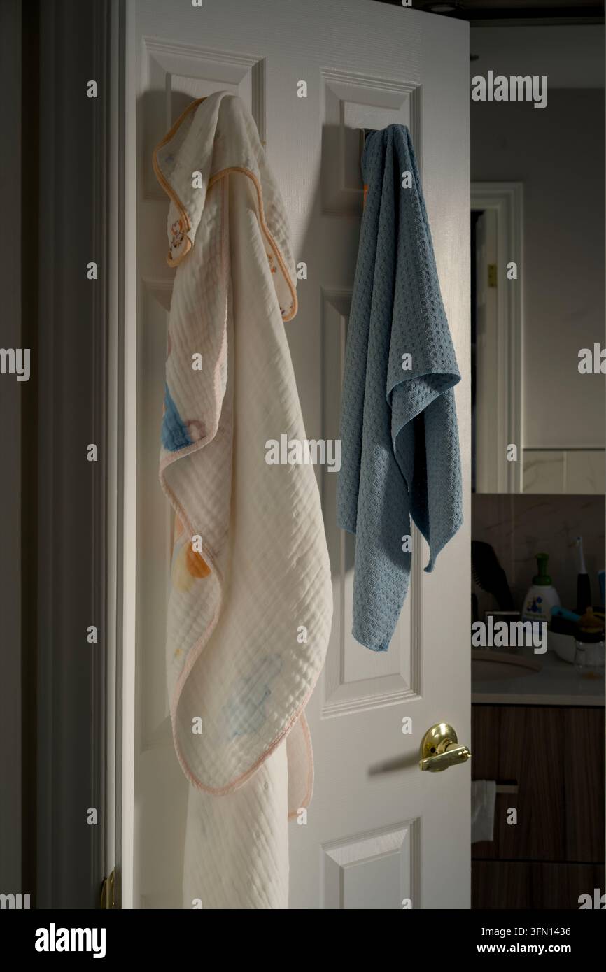 Weiße und blaue Handtücher, die an Haken einer Badezimmertür hängen Stockfoto