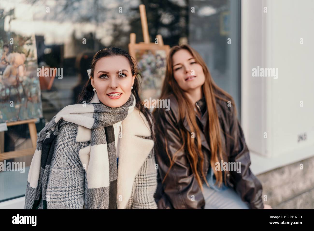 Freundinnen Kunst zwei junge Frauen sitzen zusammen vor einer Kunstgalerie und genießen einen sonnigen Herbsttag in der Stadt Stockfoto