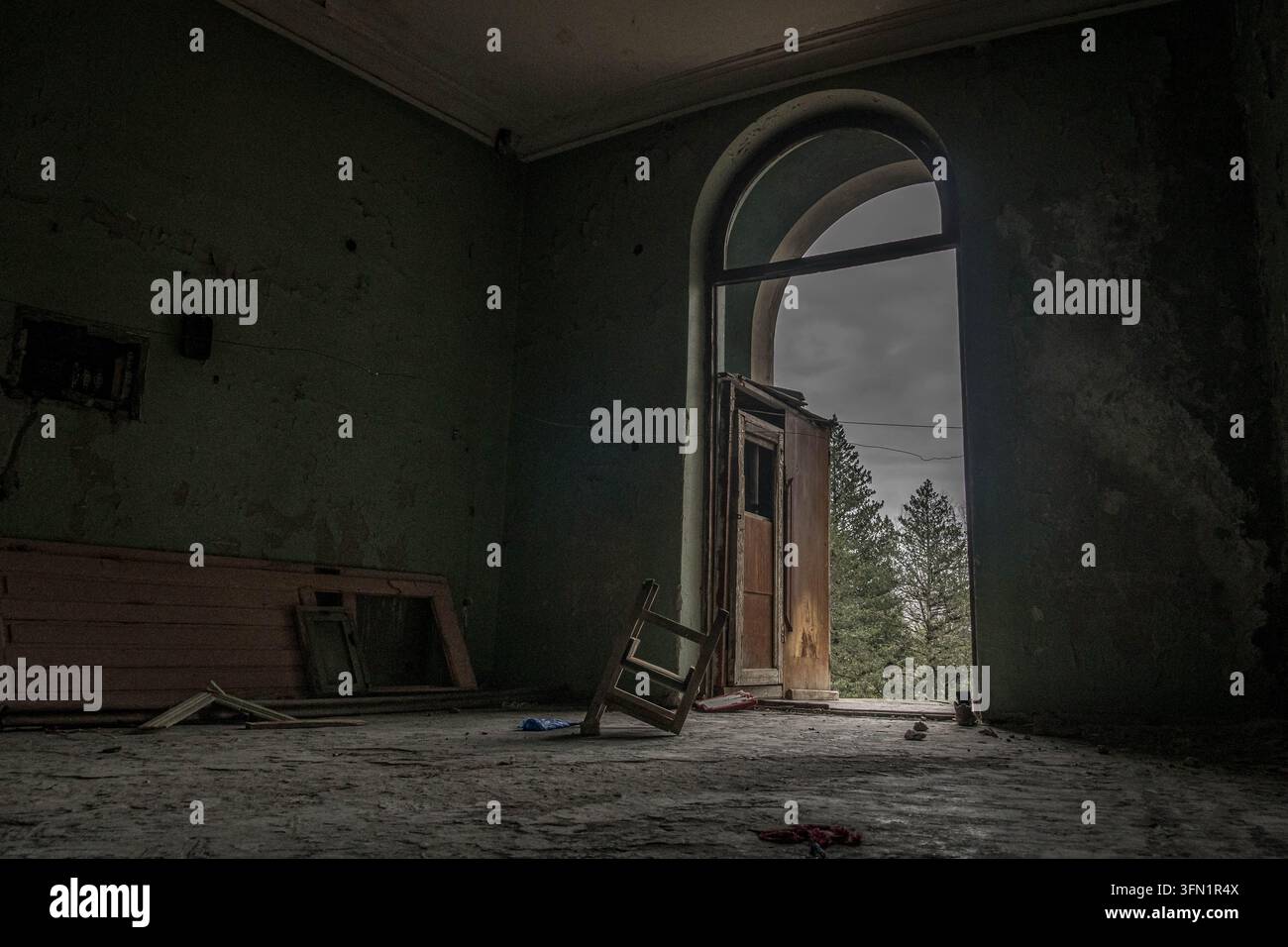 Innenraum eines verlassenen Sanatoriums in Tskaltubo, Georgien, mit einem einsamen Stuhl, umgeben von vergessenen Gegenständen in einem stillen, leeren Raum. Stockfoto