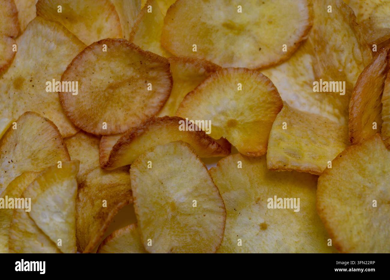 Vollbild-Nahaufnahme von knusprig gebratenen Kassava-Chips mit goldenen Rändern und Gewürzpunkten, sich überlappende Scheiben Stockfoto