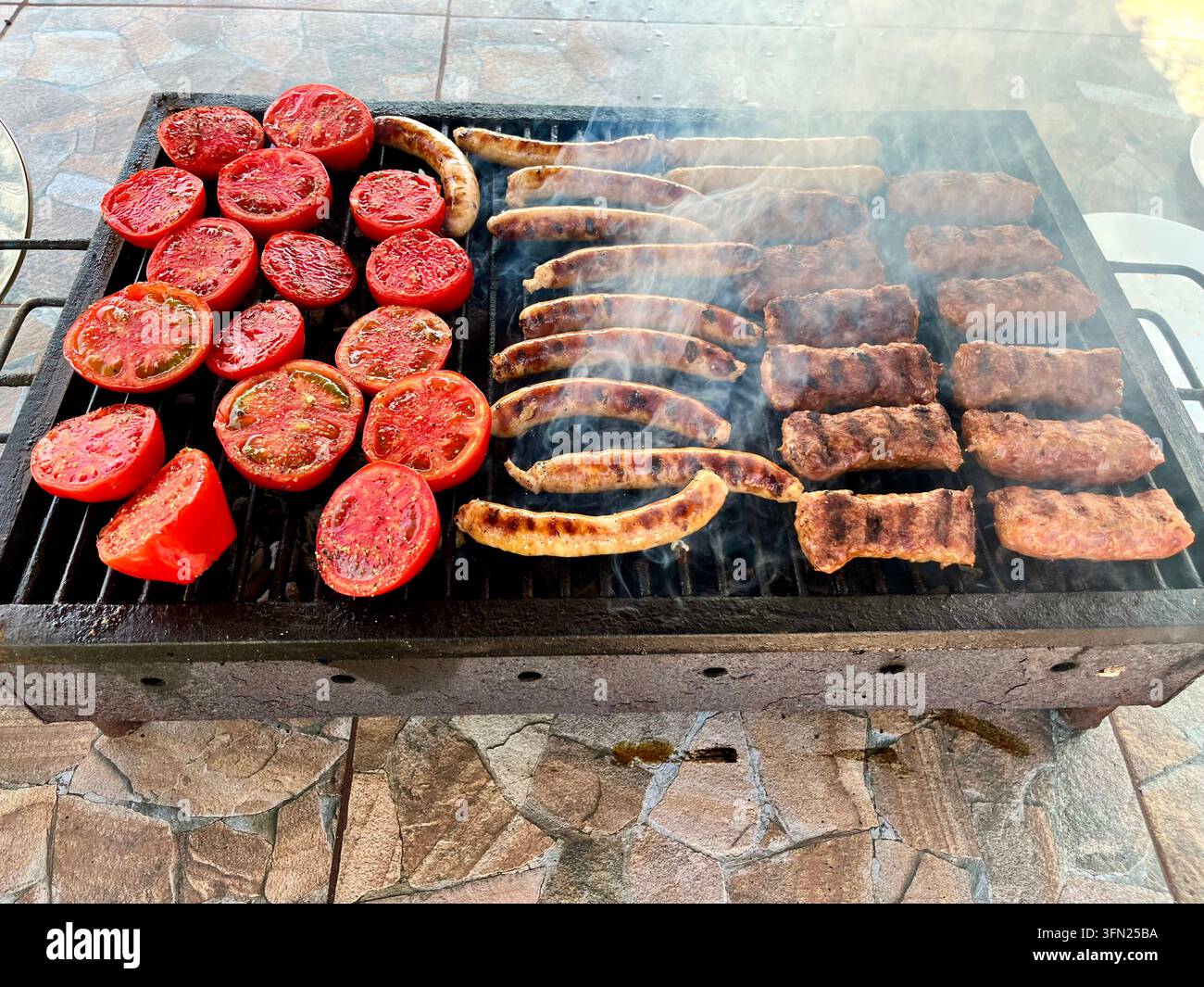 Traditionelles rumänisches Barbecue mit gegrillten Mici, Würsten und frischen Tomaten - Smartphone-aufgenommenes Stockfoto
