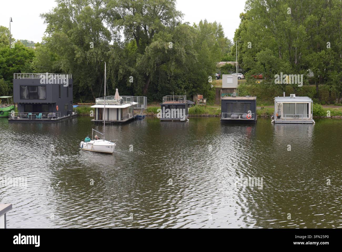 Menschen in einem kleinen Boot, das an den ehemaligen Docks der Moldau angebundene Hausboote passiert, Prag, Tschechische Republik, Juni 2026 Stockfoto