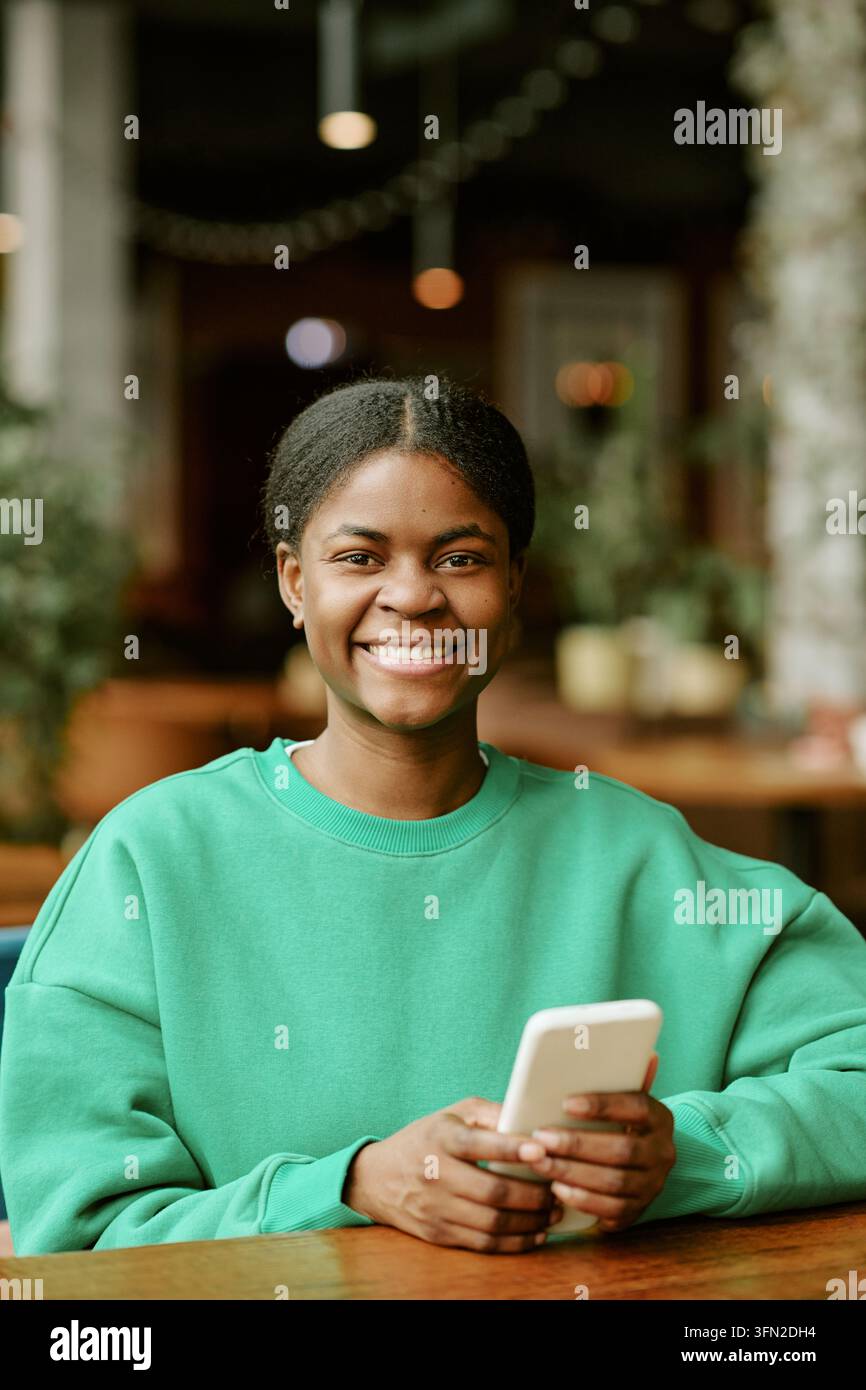 Porträt einer lächelnden schwarzen Frau, die im Café ein Smartphone hält Stockfoto