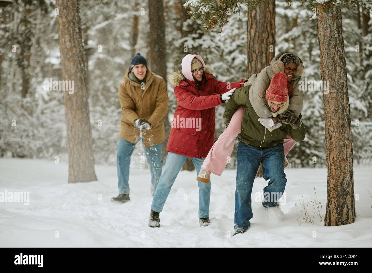 Verschiedene Freunde genießen eine Huckepackfahrt im verschneiten Winterwald Stockfoto