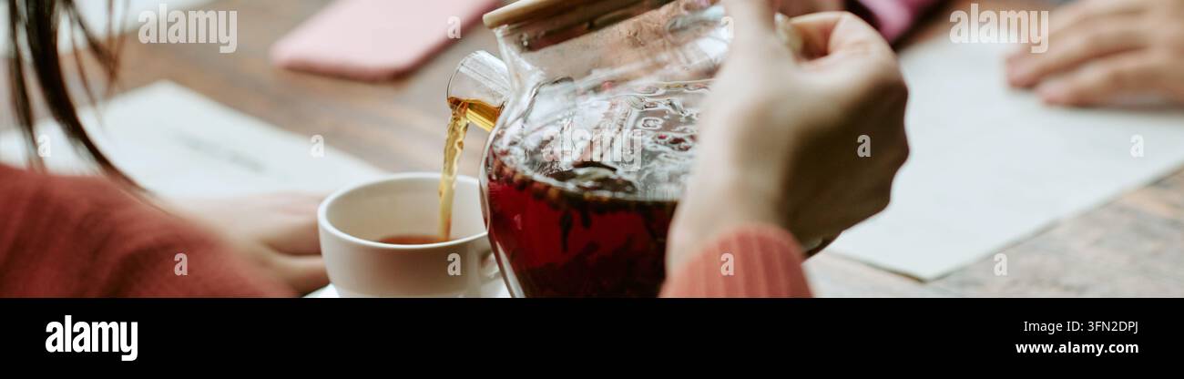 Kopfzeile der Frau, die Kräutertee in eine Tasse für verschiedene Freunde in einem Café gießt Stockfoto