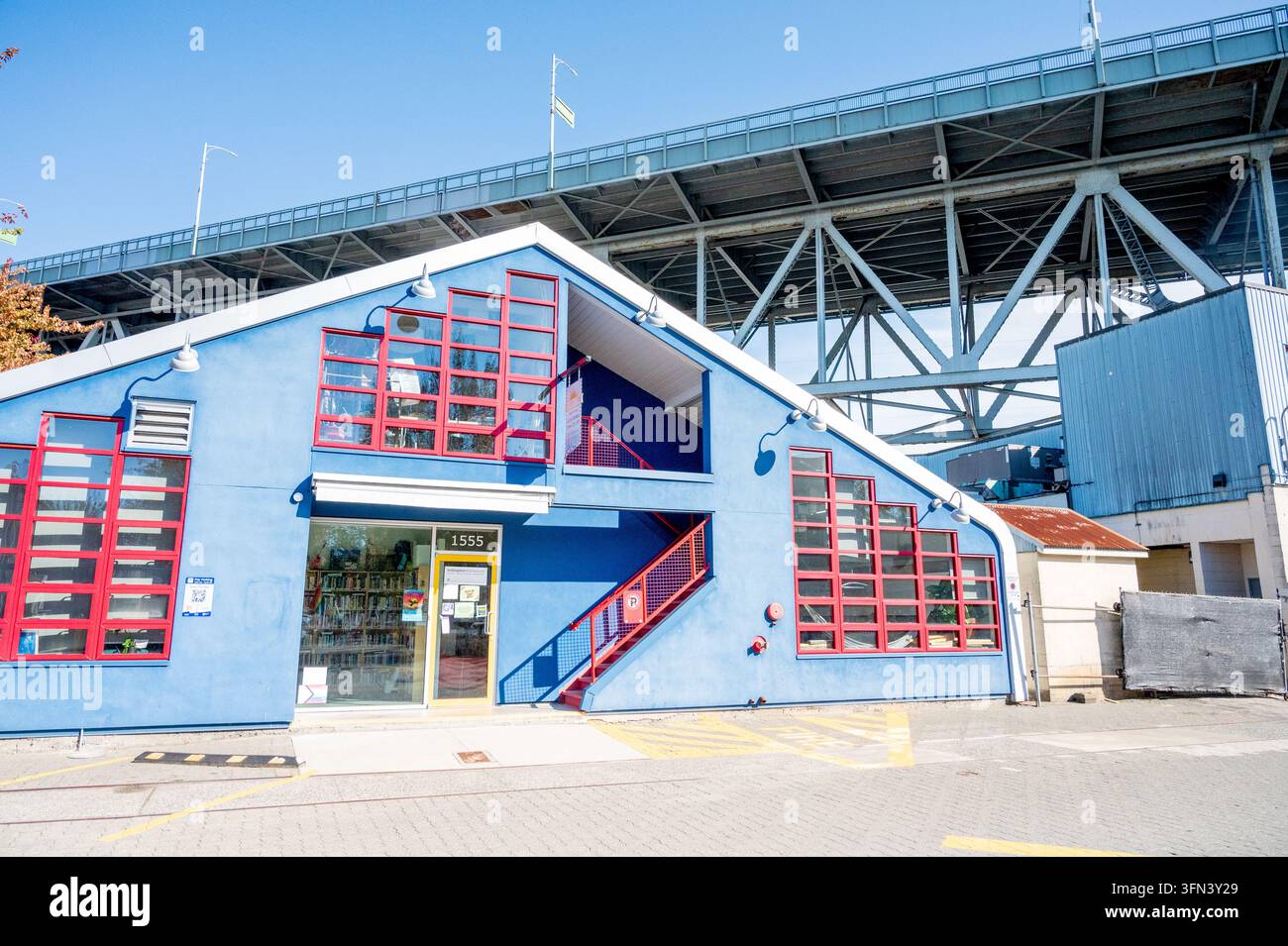 Modernes blau renoviertes Gebäude mit rot gerahmten Fenstern und Treppe unter Stahlbrückenbinder vor blauem Himmel in Vancouver. Stockfoto