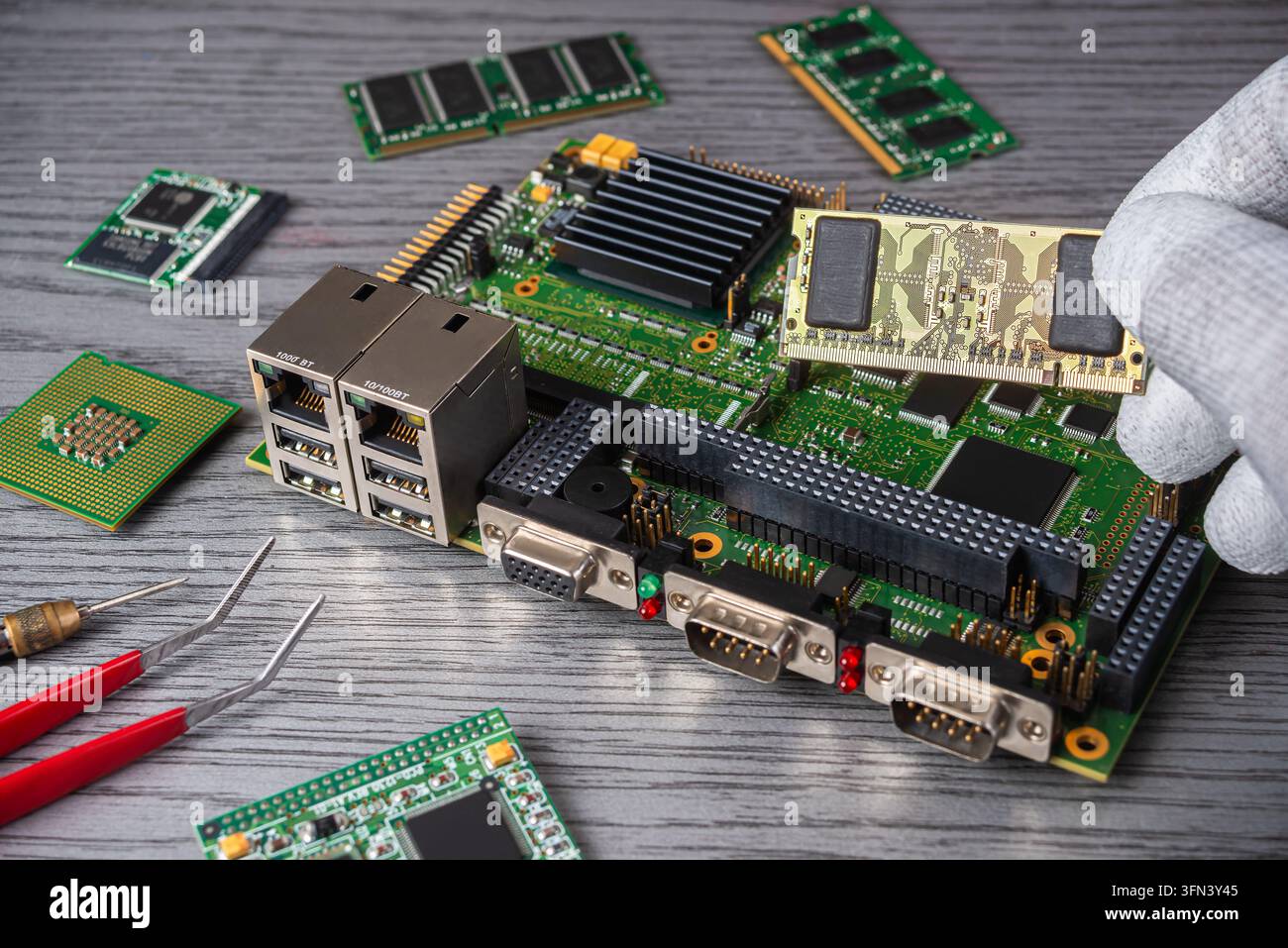 Eine Person konzentriert sich auf die Montage einer Platine, während verschiedene Computerteile auf einem Tisch in einer Werkstatt verstreut liegen. Stockfoto