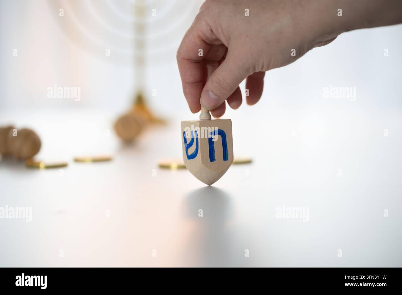 Nahaufnahme einer Hand, die einen hölzernen Chanukka-Ichtser auf einem hellen Studiotisch hält, Vorspin mit weichem, diffusem Licht und einem festlichen Blau, Weiß und Stockfoto