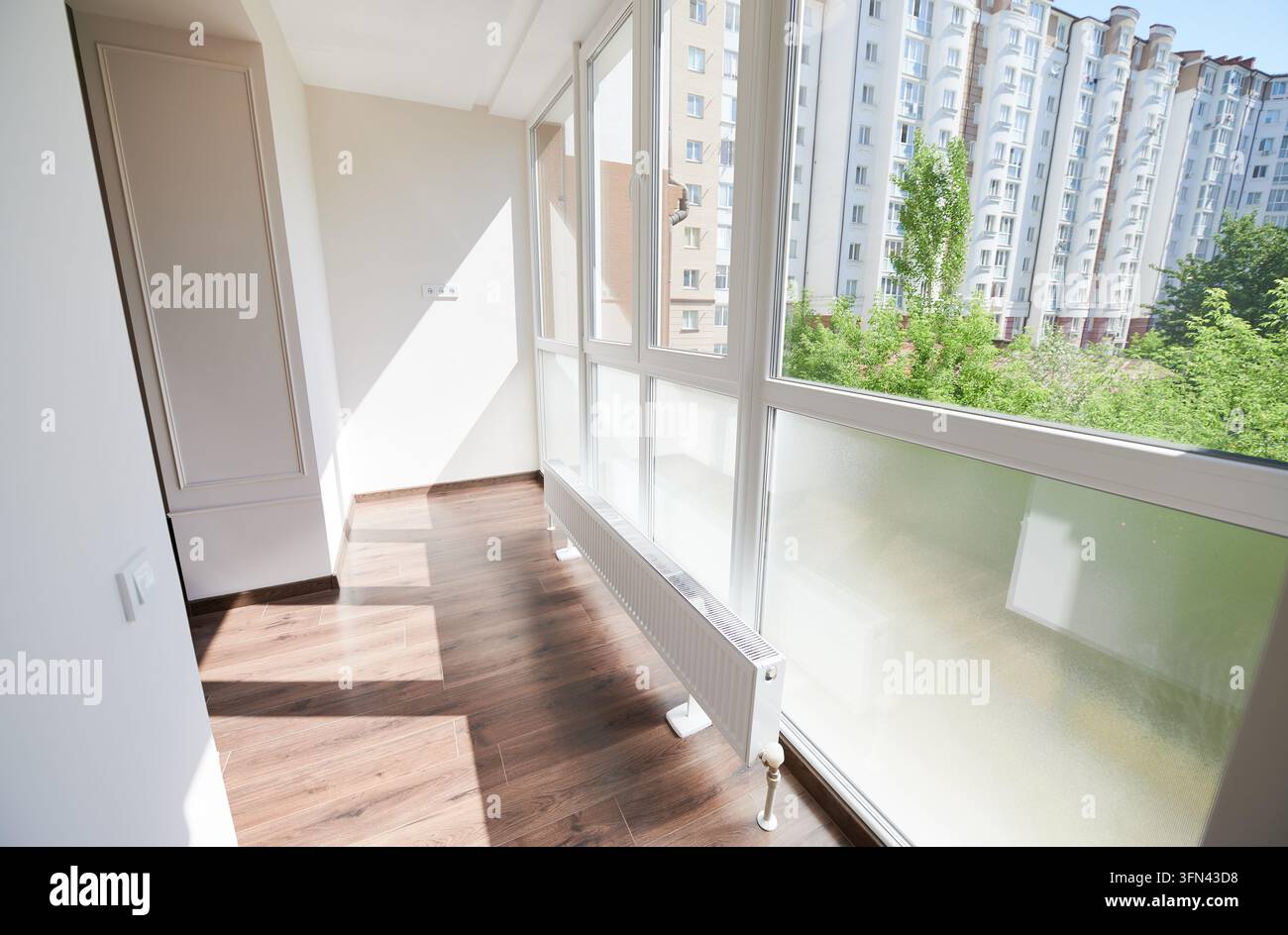 Geräumige Fensterbank mit weißem Heizkörper und weiter städtischer Aussicht, saubere Optik eines zeitgenössischen Wohninterieurs. Wohnkomfort, Isolierung und Immobilienkonzept Stockfoto