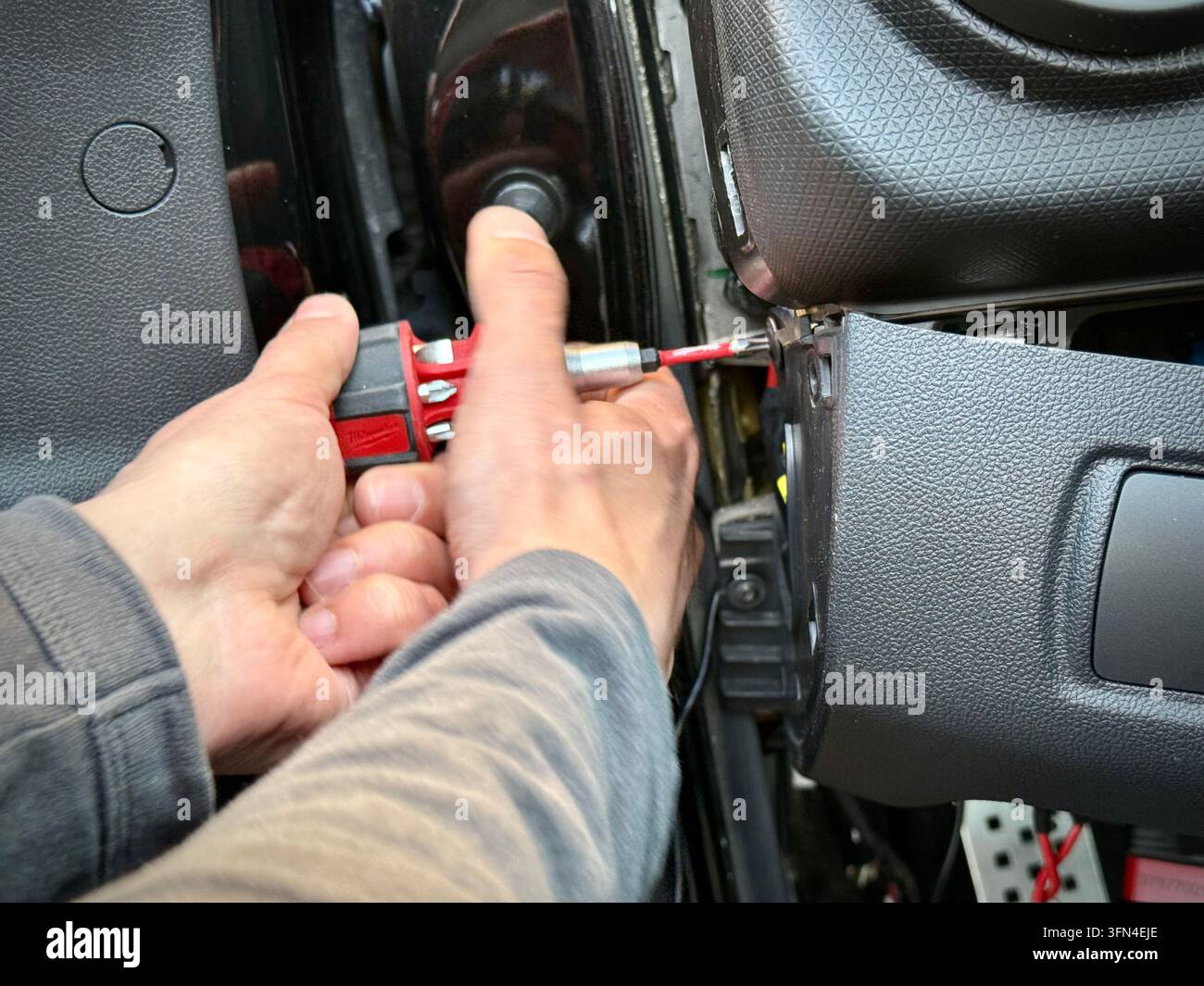 Nahaufnahme eines Mechanikers, der einen Schraubenzieher verwendet, um die innere Armaturenbrett-Seitenverkleidung eines Renault Clio RS in einer Werkstatt zu demontieren. - Smartphone-aufgenommenes Stockfoto