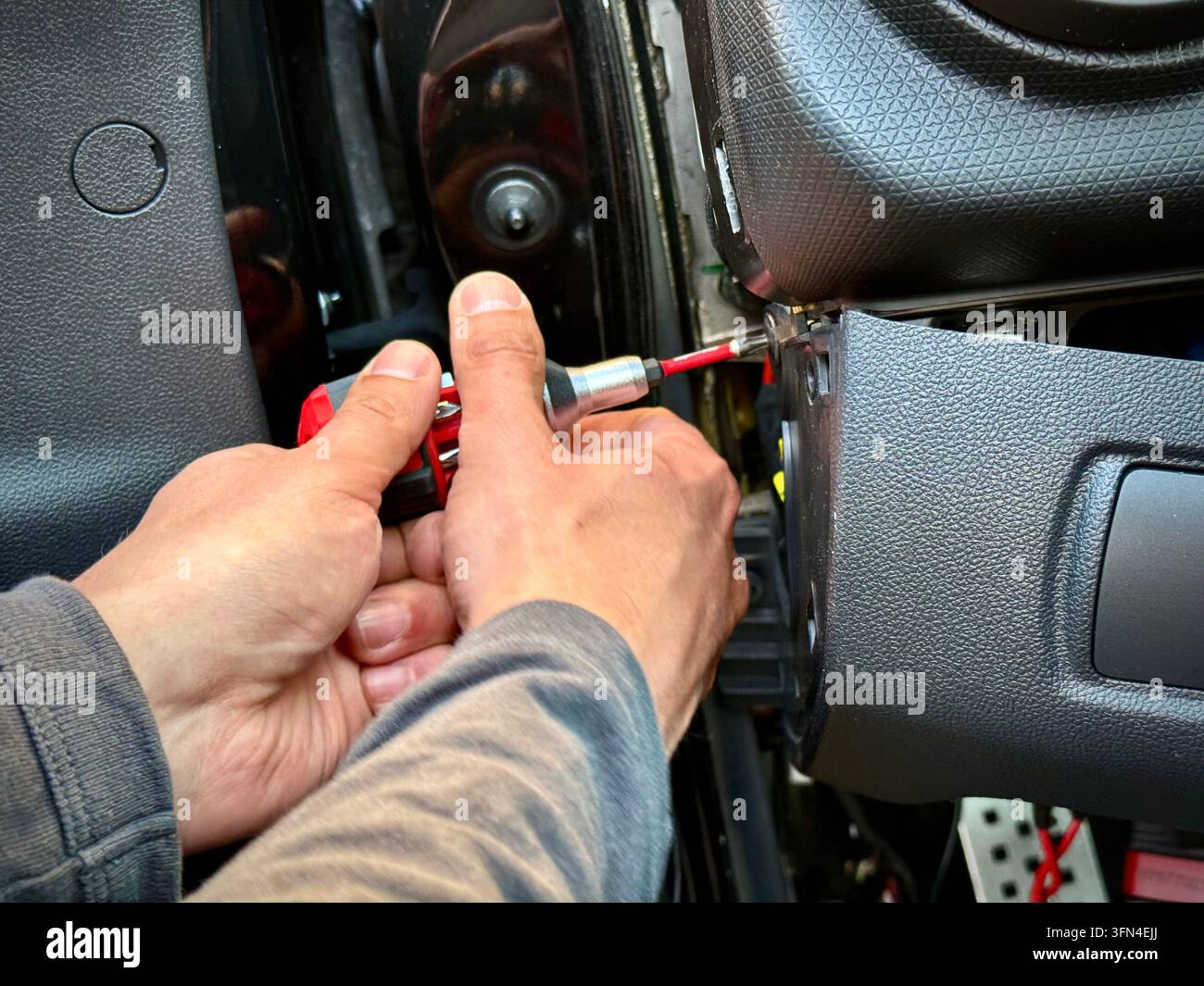 Nahaufnahme eines Mechanikers, der einen Schraubenzieher verwendet, um die innere Armaturenbrett-Seitenverkleidung eines Renault Clio RS in einer Werkstatt zu demontieren. - Smartphone-aufgenommenes Stockfoto