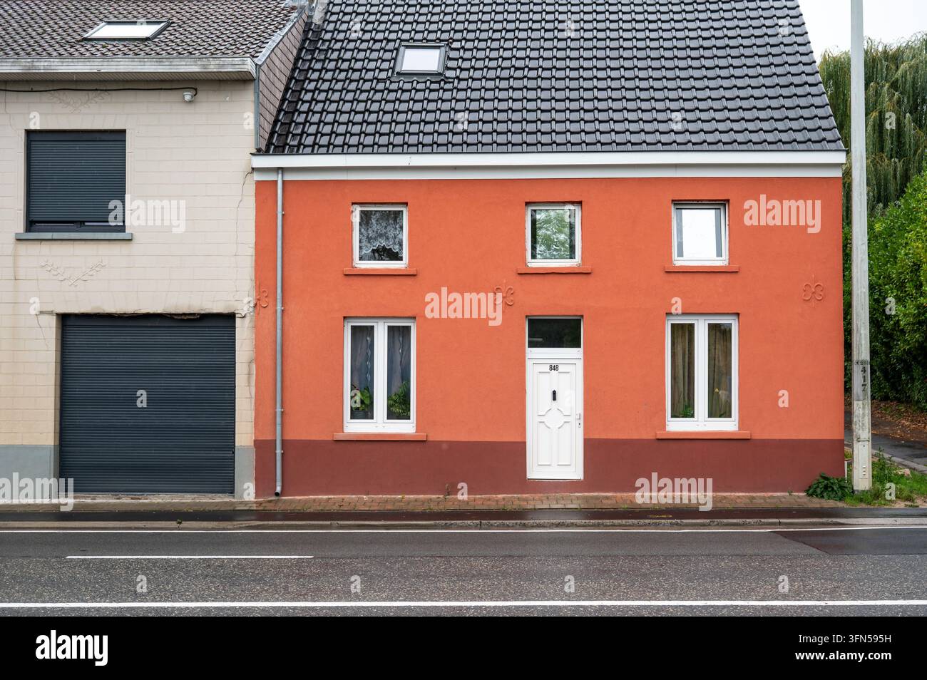 Eine Reihe einfacher Reihenhäuser entlang der Ninove-Straße in Dilbeek bei Regenwetter. Die Wohnhäuser sind Teil der dichten Straßenbebauung Stockfoto