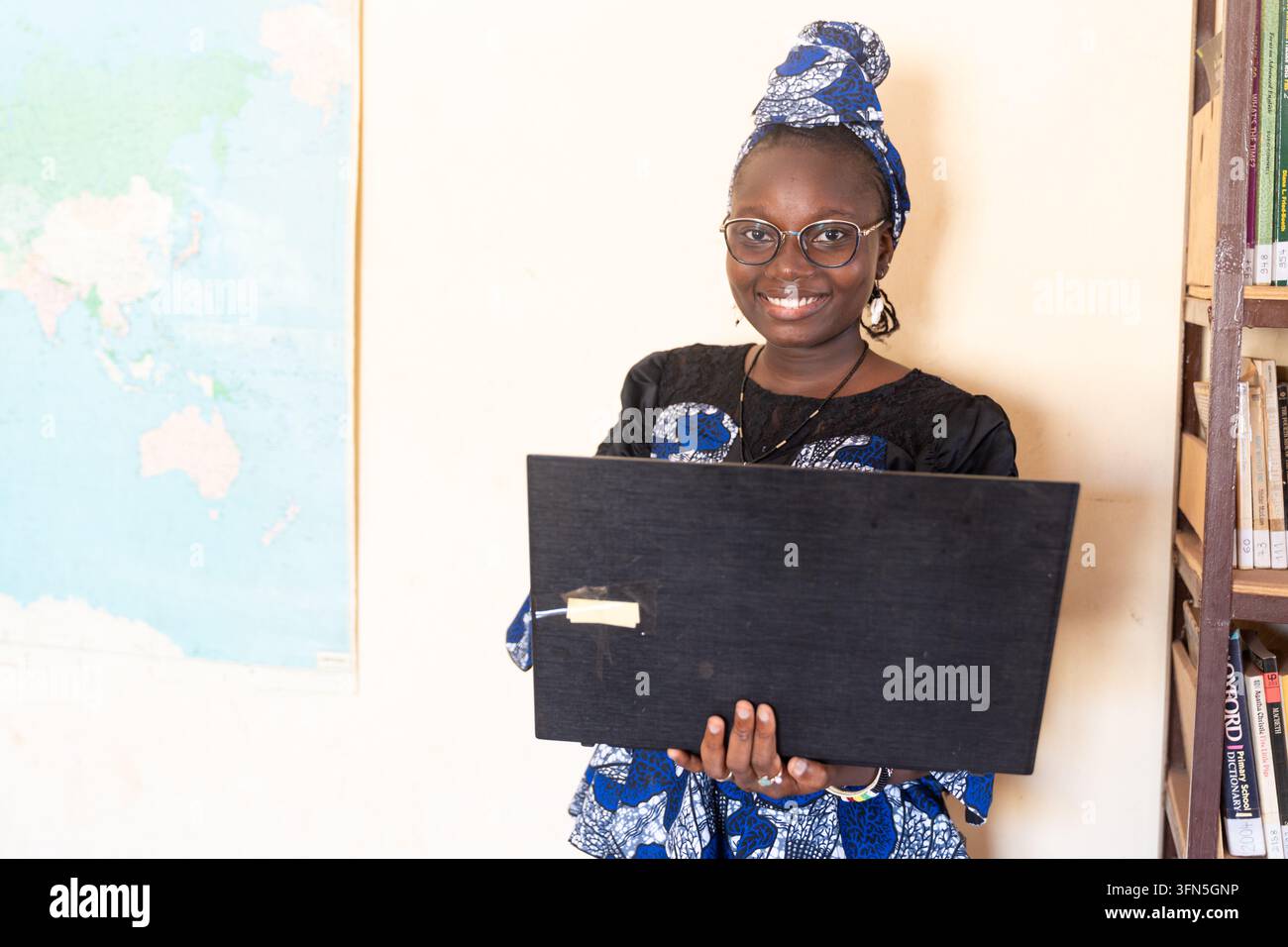 Selbstbewusste afrikanische Frau hält einen offenen Laptop in einer Bibliothek und vereint Technologie, Bildung, digitale Inklusion, Karriereentwicklung und Frauenberufe Stockfoto
