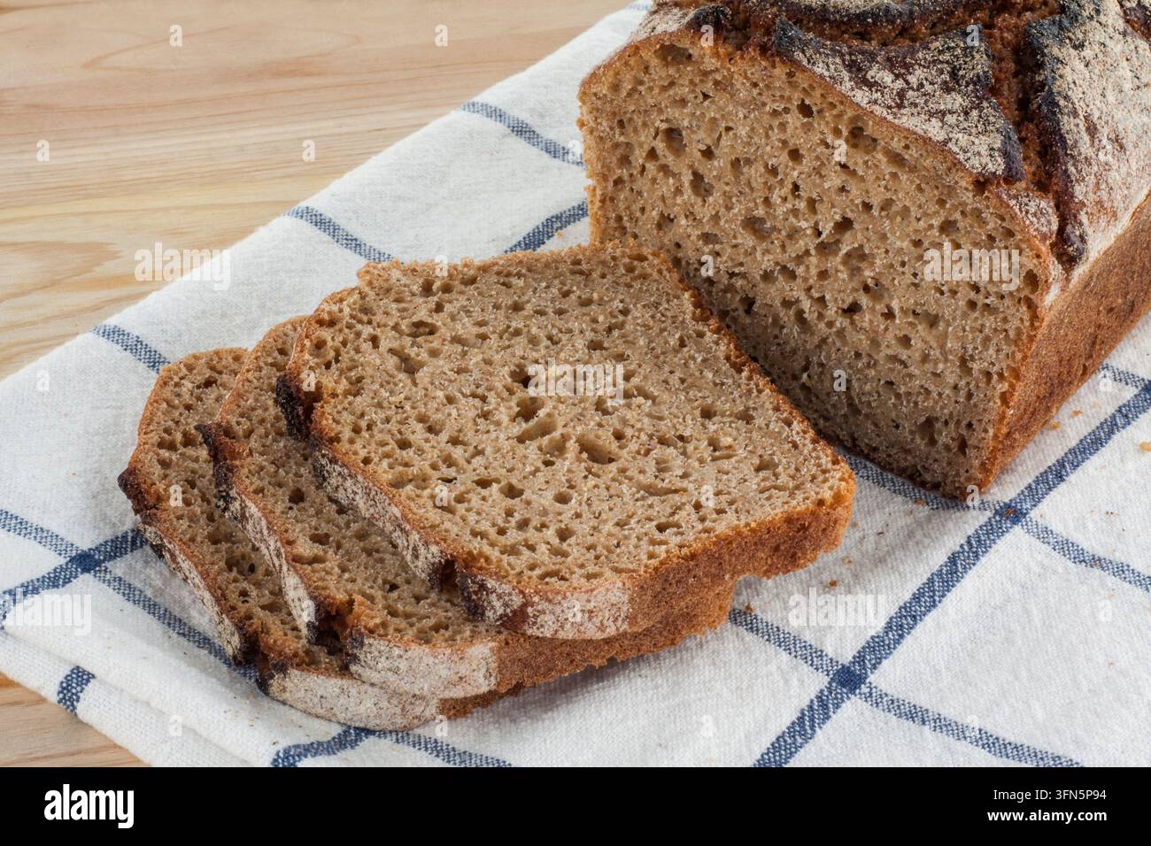Geschnittenes hausgemachtes dunkles Dinkelbrot, das auf einem Küchentuch auf einem Tisch angeordnet ist. Stockfoto