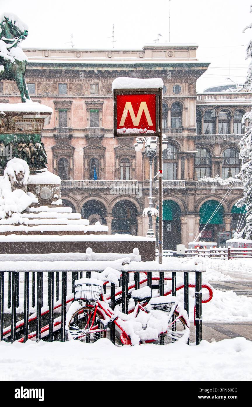 Eine vertikale Nahaufnahme zeigt das berühmte rote Schild mit dem Buchstaben M der Mailänder U-Bahn, das im Schnee versunken ist. Darunter sind schneebedeckte Fahrräder geparkt Stockfoto