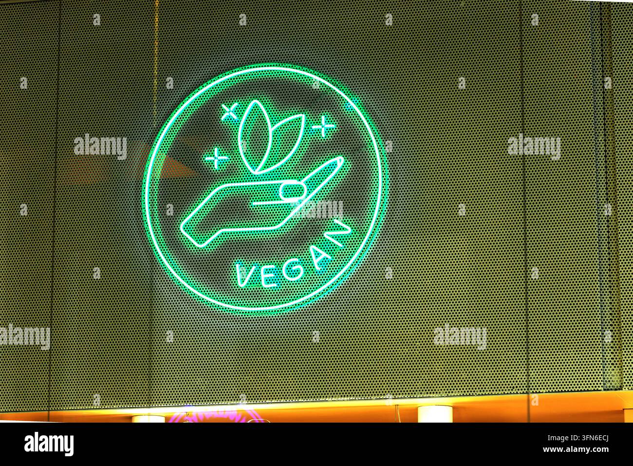 Grünes Neonzeichen mit Blatthand-Symbol und veganem Text auf Netzwand Stockfoto