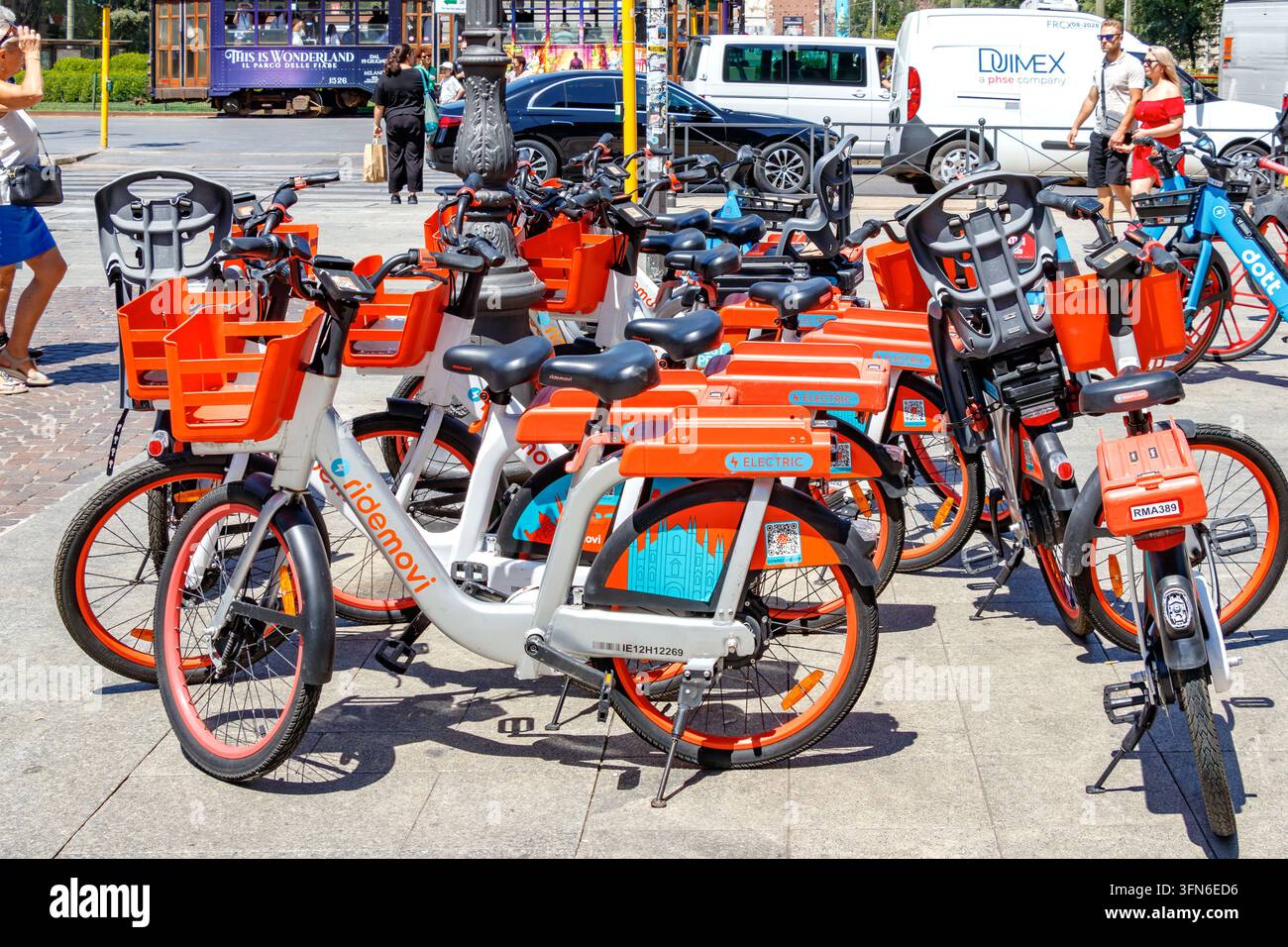 RideMovi orange und weiße Mietfahrräder, die auf der Straße in Mailand, Italien, geparkt sind, mit Dott-Fahrrad und Straßenbahn im Hintergrund Stockfoto