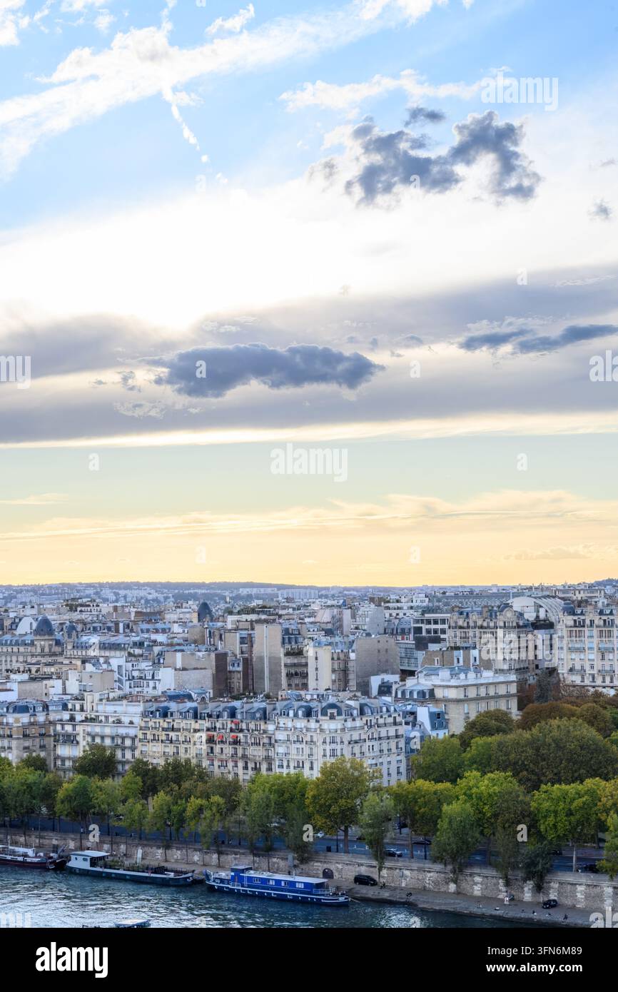 Pariser Skyline in sanftem Dämmerungslicht getaucht. Die Seine fließt sanft unter baumbewachsenen Ufern. Die Stadtlandschaft erstreckt sich mit Dächern und fernen Türmen. Der Himmel hält Stockfoto