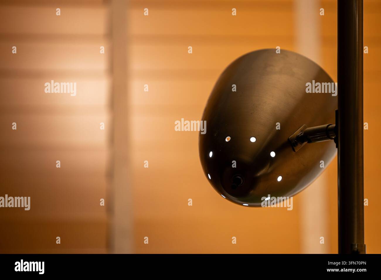 Metallischer Lampenschirm erstreckt sich in ein sanft beleuchtetes Interieur mit warmem bernsteinfarbenem Licht und großzügigem Negativraum. Stockfoto