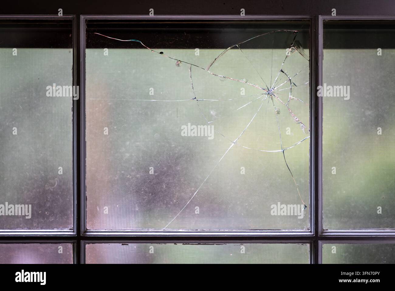 Zersplittertes und rissiges Glas in einem geteilten Wohnfenster mit strahlenförmigen Brüchen und fehlendem Glas nahe der Oberkante. Stockfoto