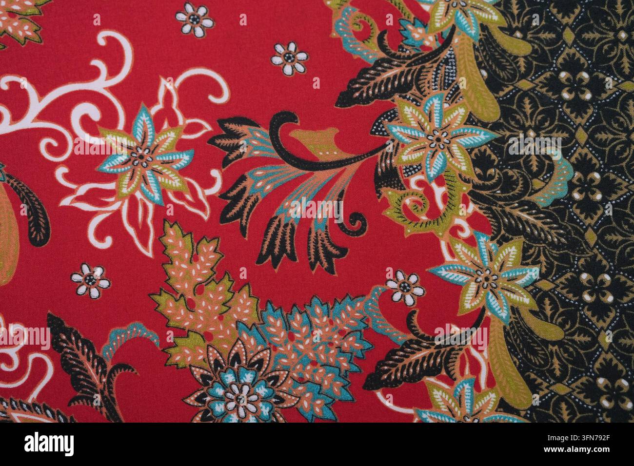 Traditionelles malaysisches rotes Batik-Textil mit kunstvollem Blumenmuster und weicher Stofftextur. Stockfoto